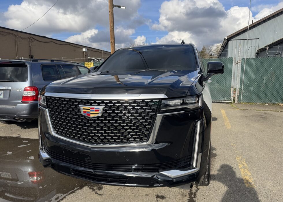 Front view of a black luxury Cadillac Escalade with a chrome mesh grille and LED headlights parked at D&R Auto Body & Paint.