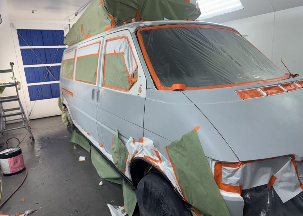 A silver Volkswagen EuroVan T4 masked with green paper and orange tape for a professional paint job inside the D&R Auto Body & Paint spray booth.