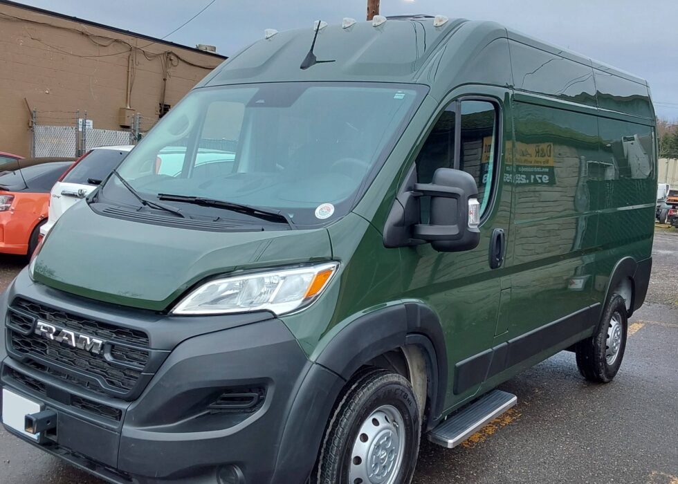 Dark green RAM ProMaster cargo van parked outside D & R Autobody after body repair and paint service.