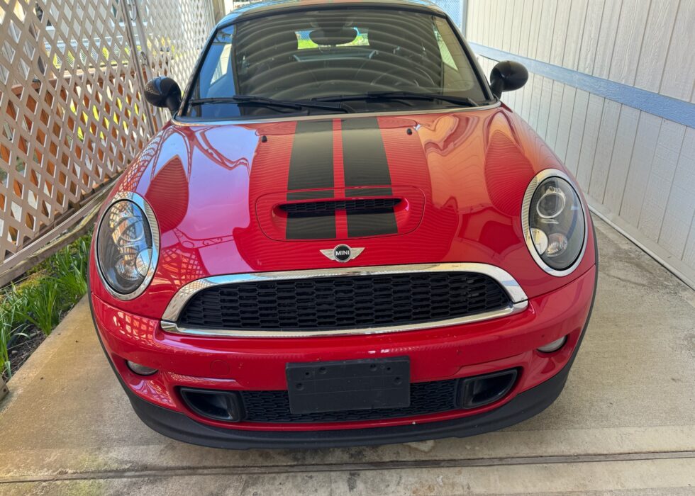 Front view of a red MINI Cooper S with black hood racing stripes and chrome grille details parked at D&R Auto Body & Paint.